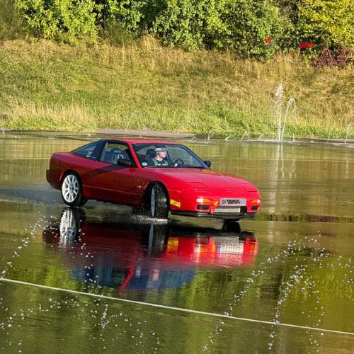 Roter Nissan beim Drifttraining am Nürburgring Basiskurs auf nasser Driftfläche mit Wasserfontäne